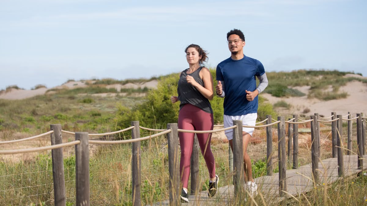 Active couple jogging on a scenic coastal boardwalk in Portugal, enjoying fitness and nature.